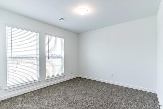 spare room with dark colored carpet and a healthy amount of sunlight