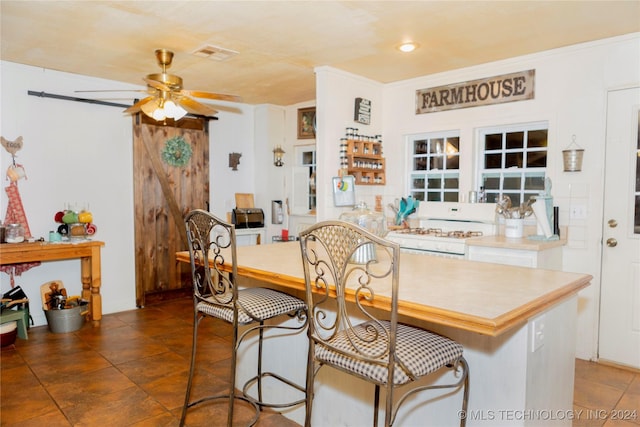 dining room featuring a barn door, ceiling fan, and ornamental molding