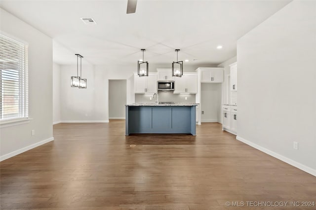 kitchen featuring light stone countertops, white cabinets, an island with sink, and hardwood / wood-style flooring