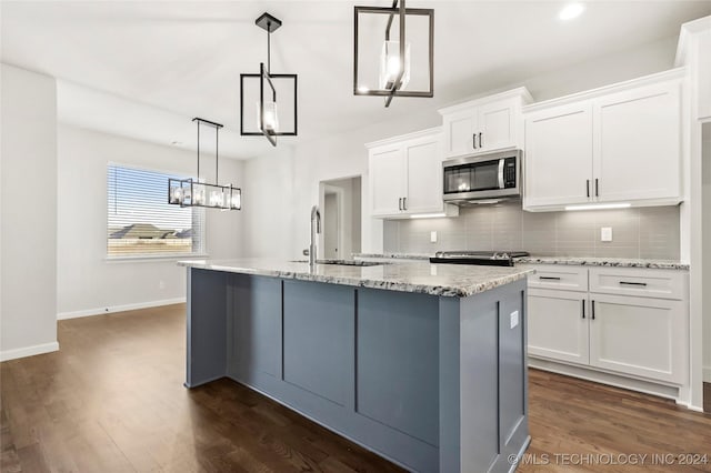 kitchen with stainless steel appliances, dark wood-type flooring, pendant lighting, a center island with sink, and white cabinetry