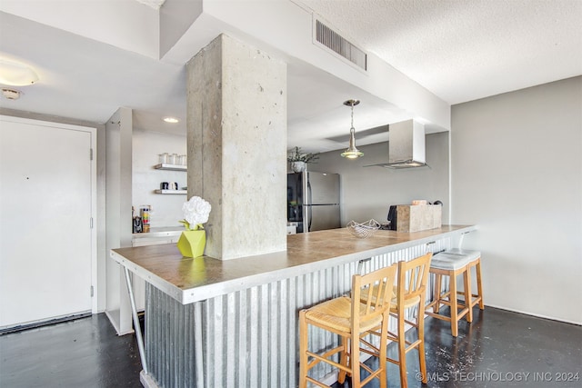 kitchen with a kitchen breakfast bar, stainless steel refrigerator, a textured ceiling, and wall chimney range hood