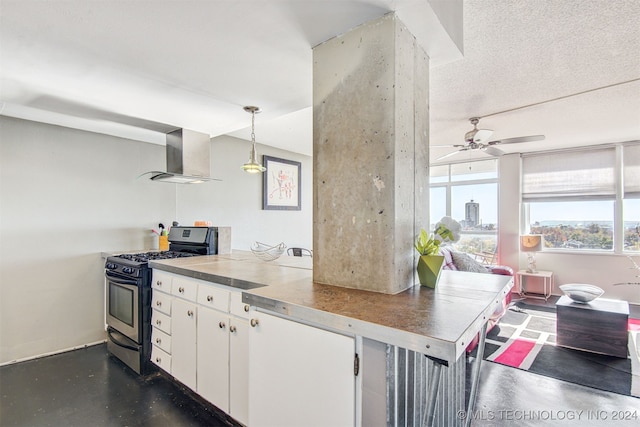 kitchen featuring white cabinets, wall chimney range hood, hanging light fixtures, gas range, and ceiling fan