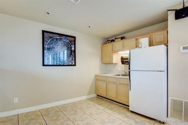 kitchen with white fridge, light tile patterned floors, sink, and light brown cabinets