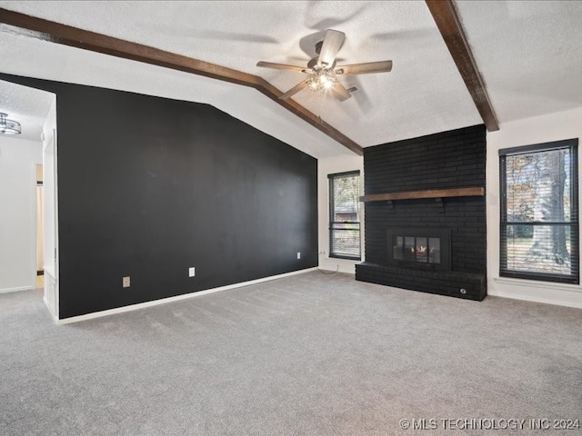 unfurnished living room with a brick fireplace, carpet flooring, vaulted ceiling with beams, ceiling fan, and a textured ceiling