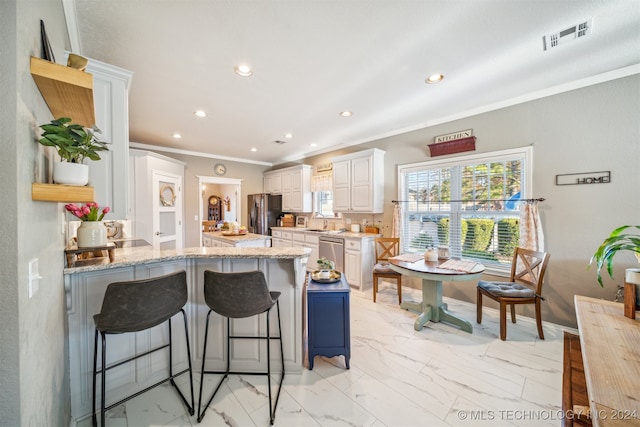 kitchen featuring a breakfast bar, white cabinets, appliances with stainless steel finishes, tasteful backsplash, and light stone counters