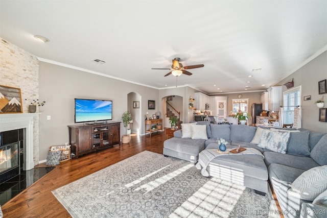 living room with ornamental molding, ceiling fan, dark wood-type flooring, and a tiled fireplace