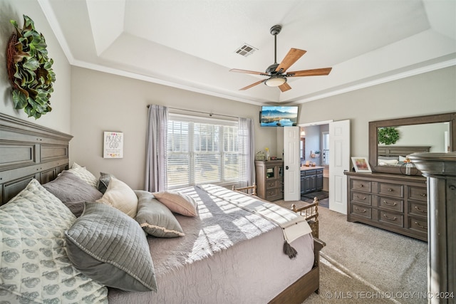 bedroom with connected bathroom, light colored carpet, a raised ceiling, and ceiling fan