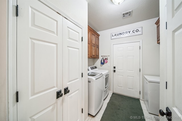 clothes washing area featuring separate washer and dryer, light tile patterned floors, cabinets, and a textured ceiling