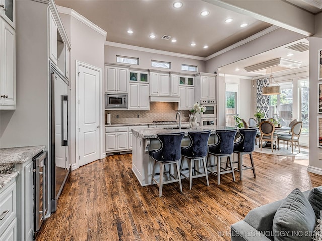 kitchen with built in appliances, white cabinets, light stone counters, and hanging light fixtures