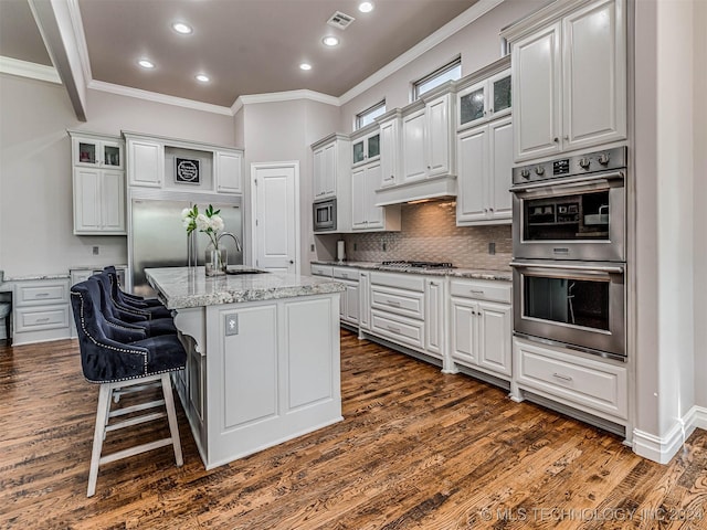 kitchen featuring white cabinetry, built in appliances, a kitchen island with sink, and light stone counters