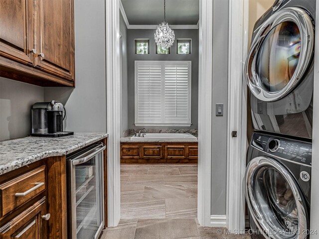 laundry room with wine cooler, crown molding, a chandelier, and stacked washer and clothes dryer