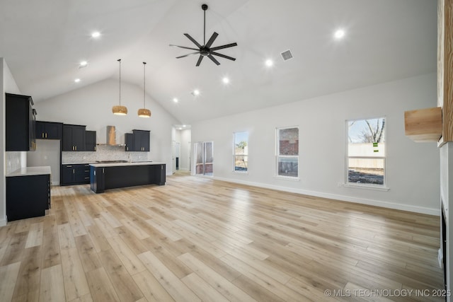 kitchen with open floor plan, high vaulted ceiling, dark cabinetry, and decorative backsplash