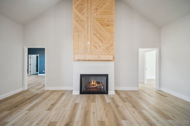 unfurnished living room featuring high vaulted ceiling, a lit fireplace, and wood finished floors