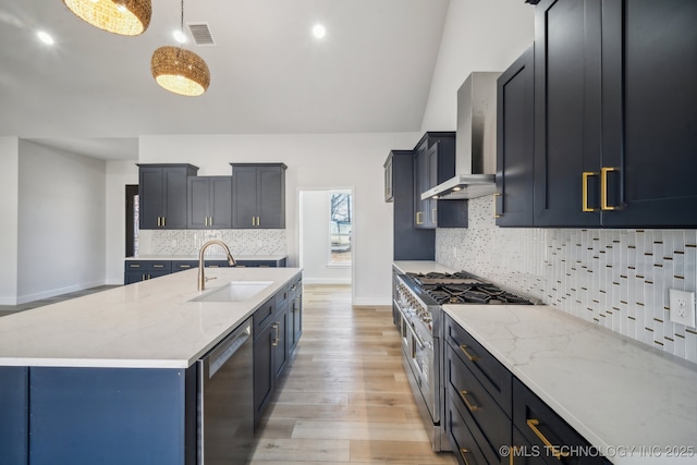 kitchen with wall chimney exhaust hood, light stone countertops, stainless steel appliances, light wood-style floors, and a sink