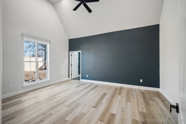 empty room featuring high vaulted ceiling, baseboards, and light wood finished floors