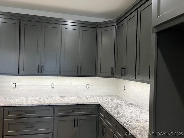 kitchen featuring gray cabinets, backsplash, and light stone counters