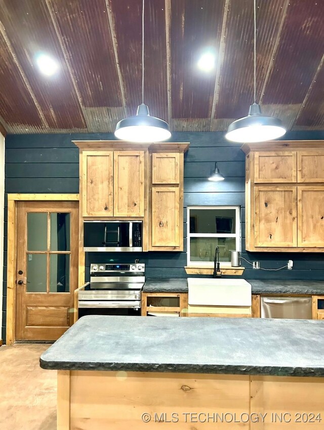 kitchen with pendant lighting, stainless steel appliances, wood walls, and sink