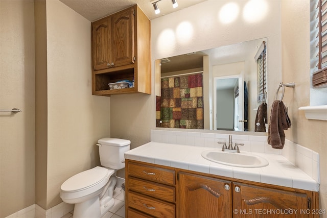 bathroom with tile patterned flooring, vanity, a textured ceiling, and toilet