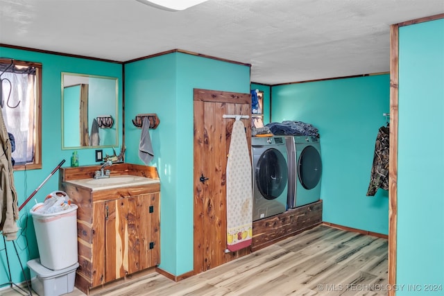 washroom featuring ornamental molding, a textured ceiling, sink, washing machine and dryer, and light hardwood / wood-style floors