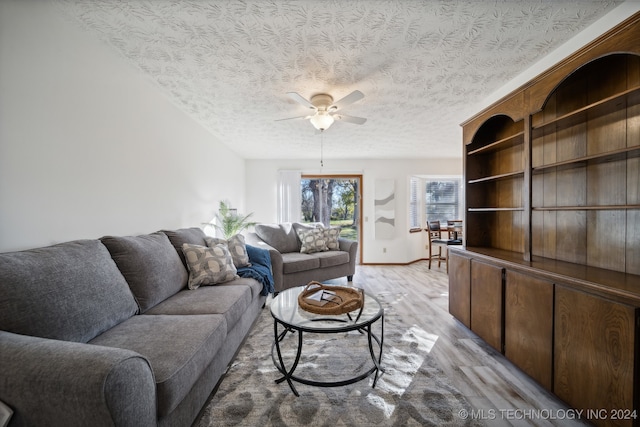 living room with ceiling fan, light wood-type flooring, and a textured ceiling