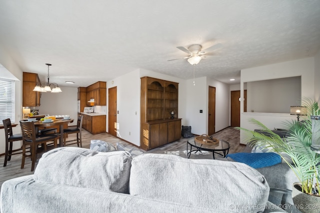 living room with a textured ceiling, wood-type flooring, and ceiling fan with notable chandelier