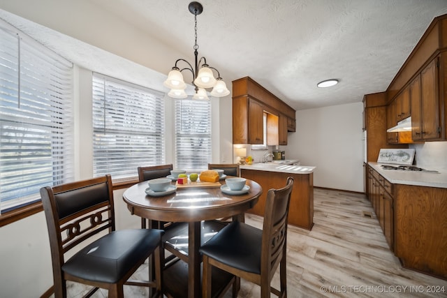 dining area with sink, light wood-type flooring, a textured ceiling, and an inviting chandelier