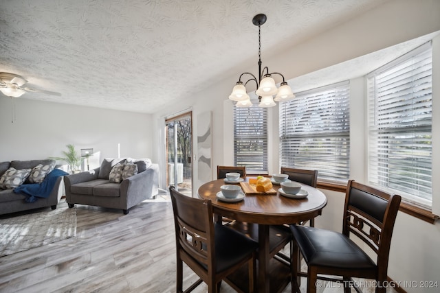 dining area with ceiling fan with notable chandelier, a textured ceiling, and light hardwood / wood-style flooring