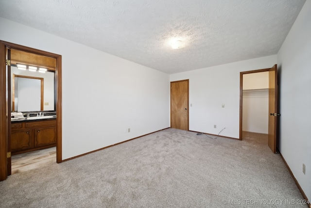 unfurnished bedroom featuring a textured ceiling, light colored carpet, and connected bathroom