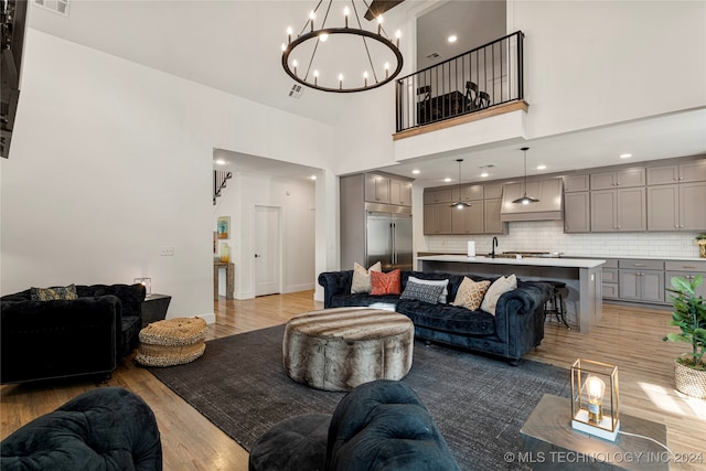 living room featuring sink, light hardwood / wood-style flooring, a high ceiling, and an inviting chandelier