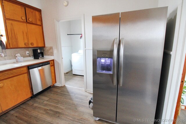 kitchen with sink, dark wood-type flooring, appliances with stainless steel finishes, tasteful backsplash, and washer / clothes dryer