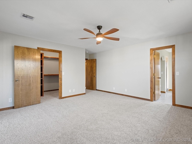 unfurnished bedroom with ceiling fan, a spacious closet, light carpet, and a closet