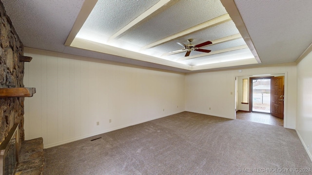 unfurnished living room with carpet floors, a raised ceiling, ceiling fan, and a stone fireplace