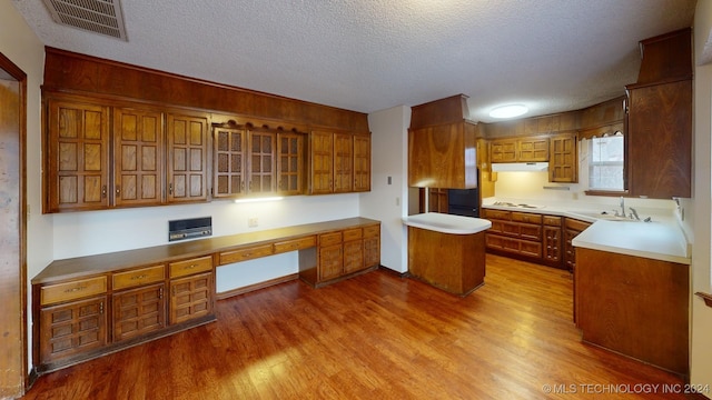 kitchen with sink, a center island, white gas stovetop, built in desk, and hardwood / wood-style flooring