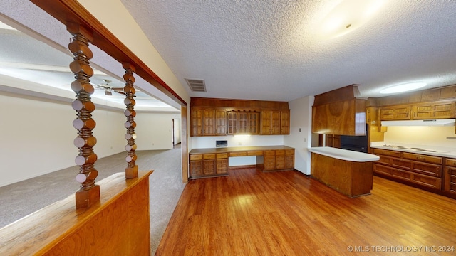 kitchen with a textured ceiling, light wood-type flooring, white cooktop, and built in desk