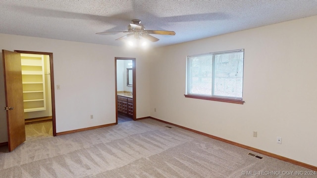 unfurnished bedroom featuring ceiling fan, a spacious closet, a textured ceiling, connected bathroom, and a closet