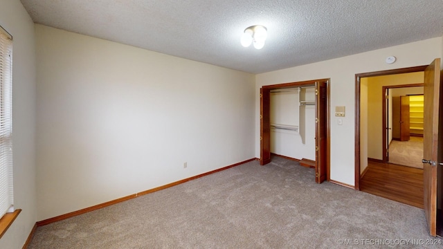 unfurnished bedroom featuring light colored carpet, a textured ceiling, and a closet