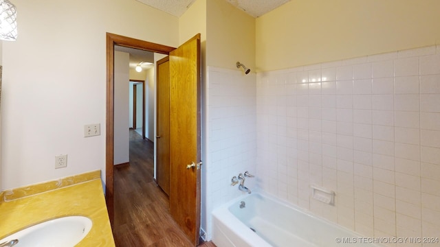 bathroom with a textured ceiling, vanity, wood-type flooring, tile walls, and tiled shower / bath