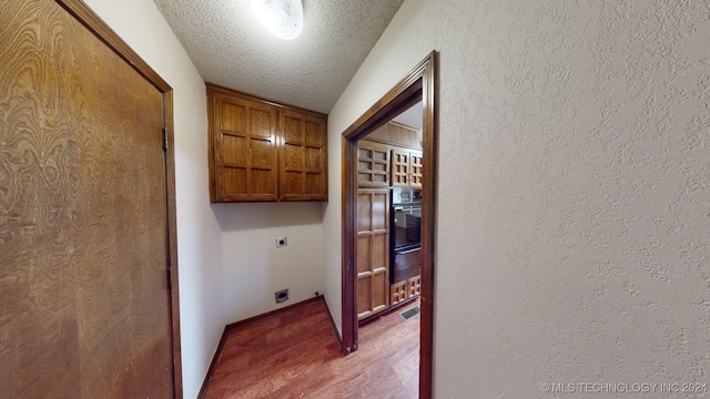 laundry room featuring hardwood / wood-style flooring, cabinets, a textured ceiling, and hookup for an electric dryer