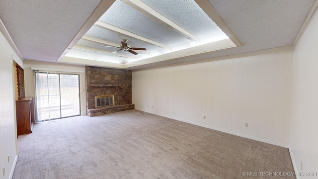 unfurnished living room with a tray ceiling, a stone fireplace, ceiling fan, and a textured ceiling