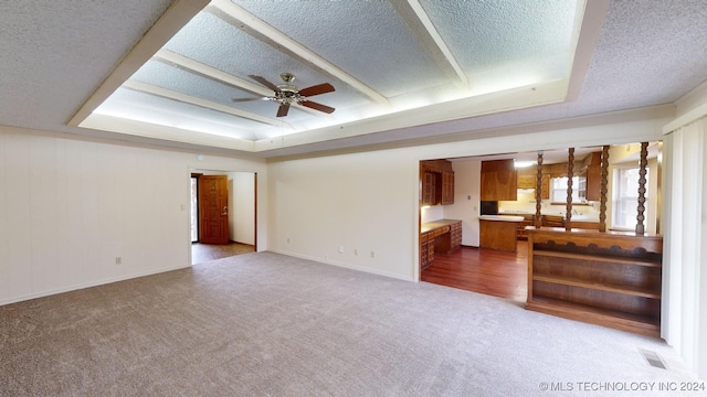 unfurnished living room featuring carpet, a textured ceiling, a tray ceiling, and ceiling fan