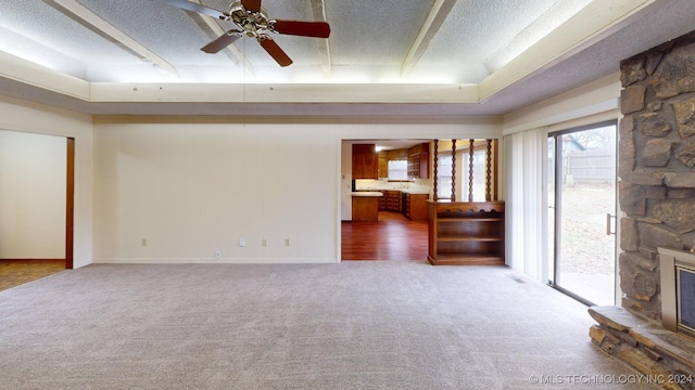 unfurnished living room with a raised ceiling, ceiling fan, a fireplace, a textured ceiling, and carpet floors