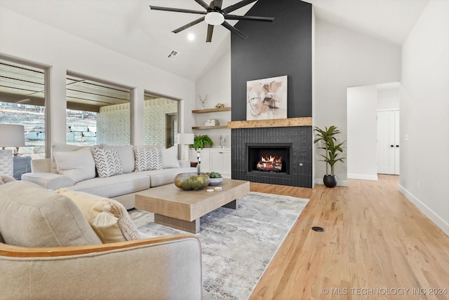 living room featuring light hardwood / wood-style flooring, high vaulted ceiling, a large fireplace, and ceiling fan