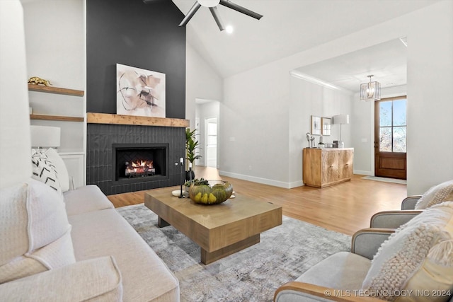 living room featuring a tile fireplace, high vaulted ceiling, ceiling fan with notable chandelier, and light hardwood / wood-style floors