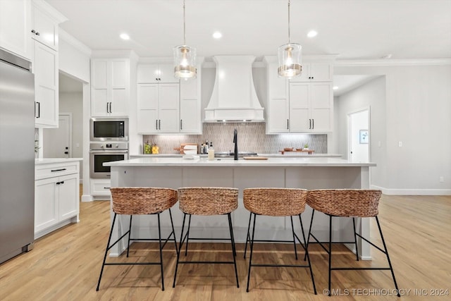 kitchen with pendant lighting, built in appliances, custom range hood, and a center island with sink