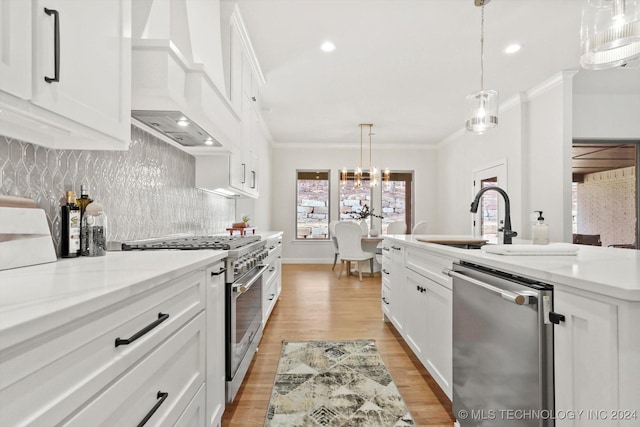 kitchen featuring sink, custom exhaust hood, white cabinetry, decorative light fixtures, and appliances with stainless steel finishes