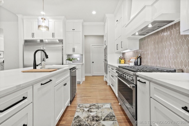 kitchen featuring built in appliances, decorative light fixtures, custom exhaust hood, and white cabinetry