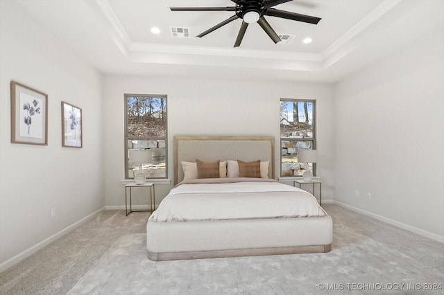 bedroom featuring light carpet, multiple windows, a raised ceiling, and ceiling fan