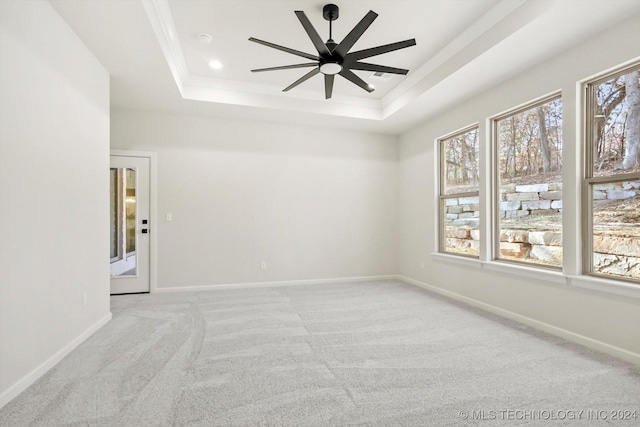 empty room with a raised ceiling, light carpet, and ceiling fan