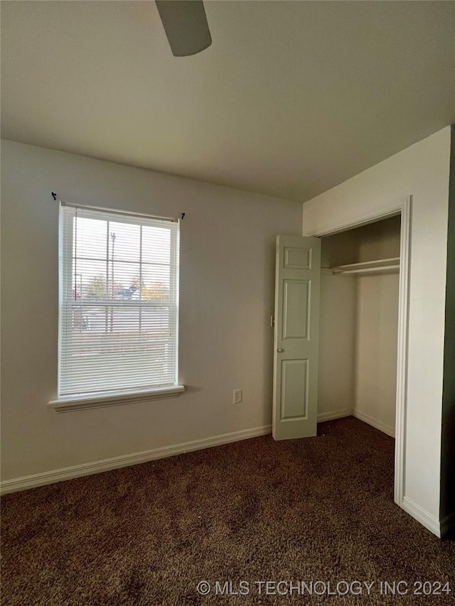 unfurnished bedroom featuring dark colored carpet, ceiling fan, and a closet