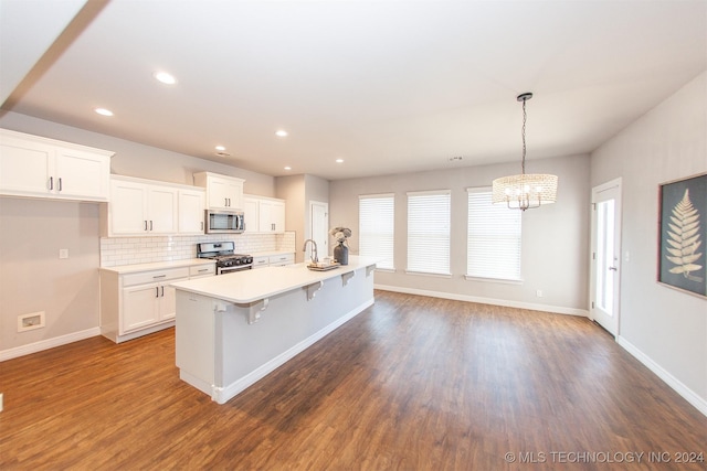 kitchen with white cabinetry, hanging light fixtures, stainless steel appliances, hardwood / wood-style floors, and a kitchen island with sink